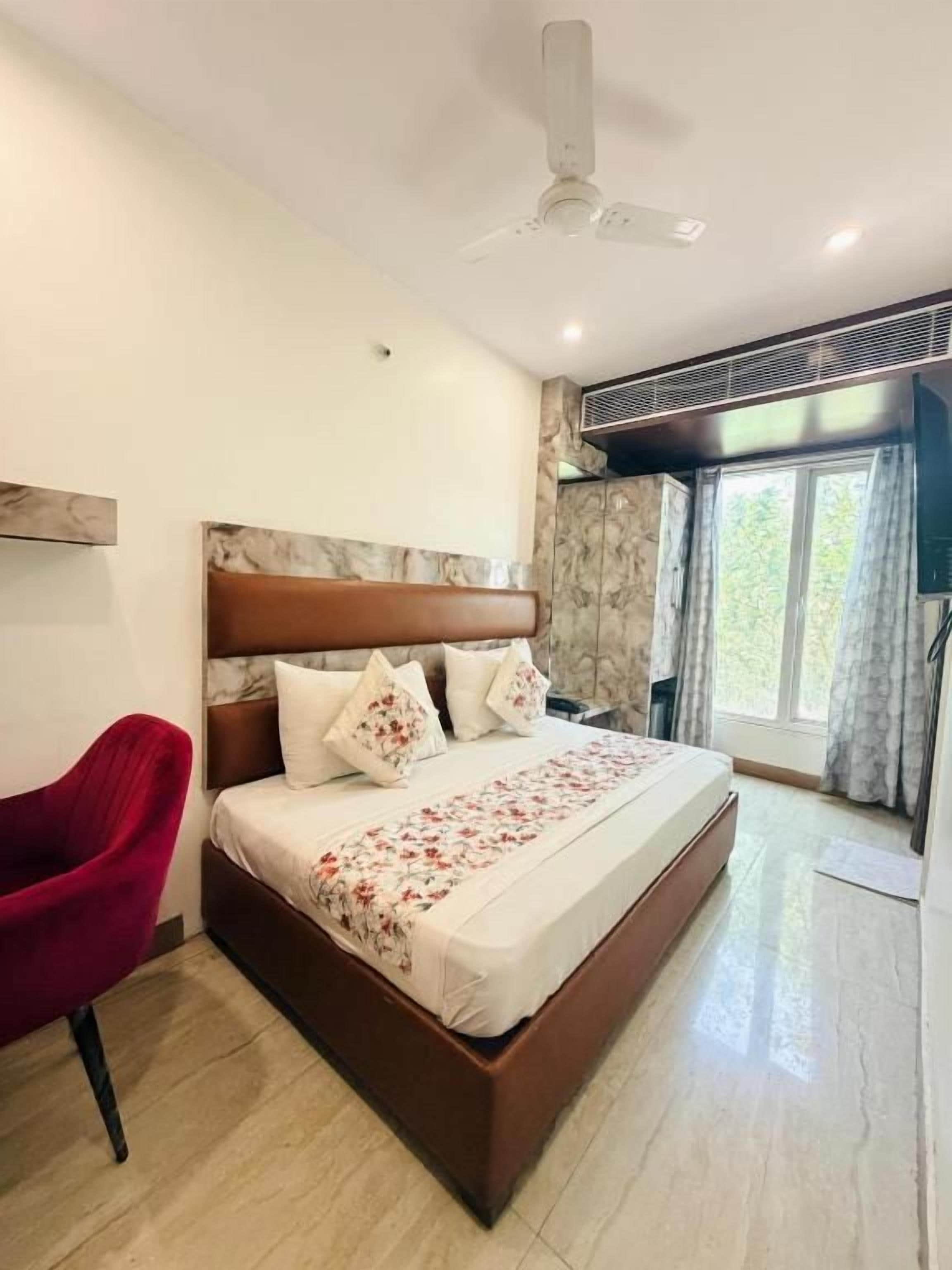 A hotel room with a bed, a red chair, a ceiling fan, and a window with curtains.