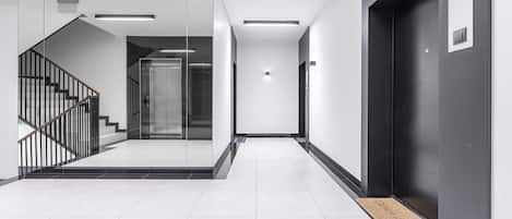 A modern interior with a staircase, elevator, and a hallway leading to an exit.