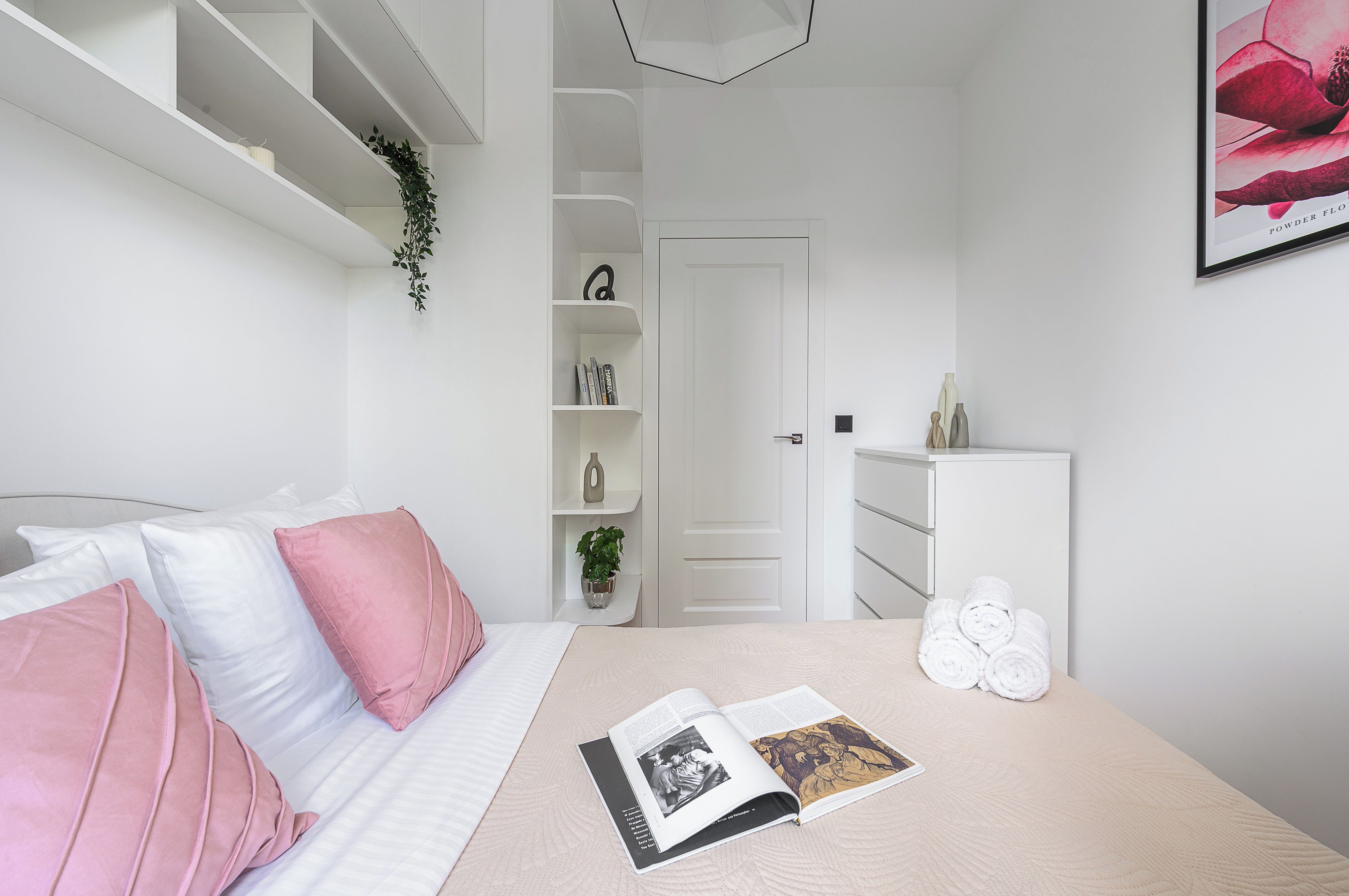 Une chambre à coucher avec un lit, une table de chevet sur laquelle se trouve un livre, une commode et une porte donnant sur une autre pièce.