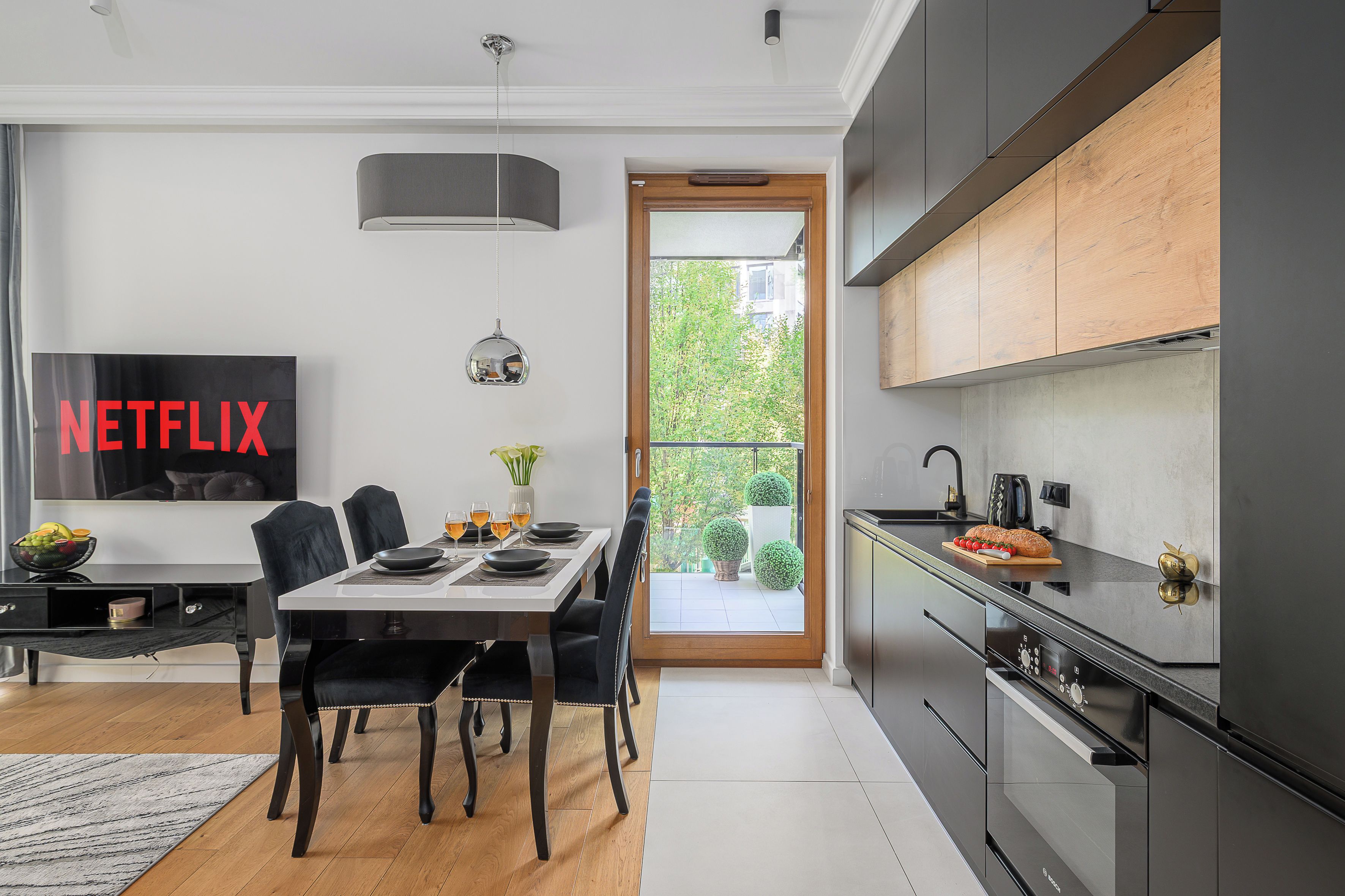 Une cuisine moderne dotée d’un four encastré, un coin repas avec une table et des chaises, et une grande fenêtre donnant sur un paysage verdoyant.