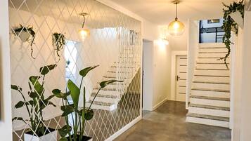Un couloir avec un mur de séparation blanc, des plantes en pot et un escalier.
