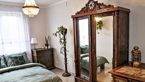 Une chambre avec un grand miroir, un lit avec une literie verte, une commode et une plante suspendue.