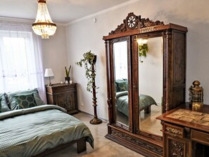 Un dormitorio con un espejo grande, una cama con ropa de cama verde, un tocador y una planta colgante.