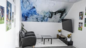 Una sala de estar moderna con un gran mural abstracto, un televisor de pantalla plana, un sofá de cuero negro, una mesita de centro pequeña y una mesa de ping pong.