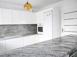 Cocina moderna con armarios blancos, encimera de granito, horno empotrado y una lámpara colgante.