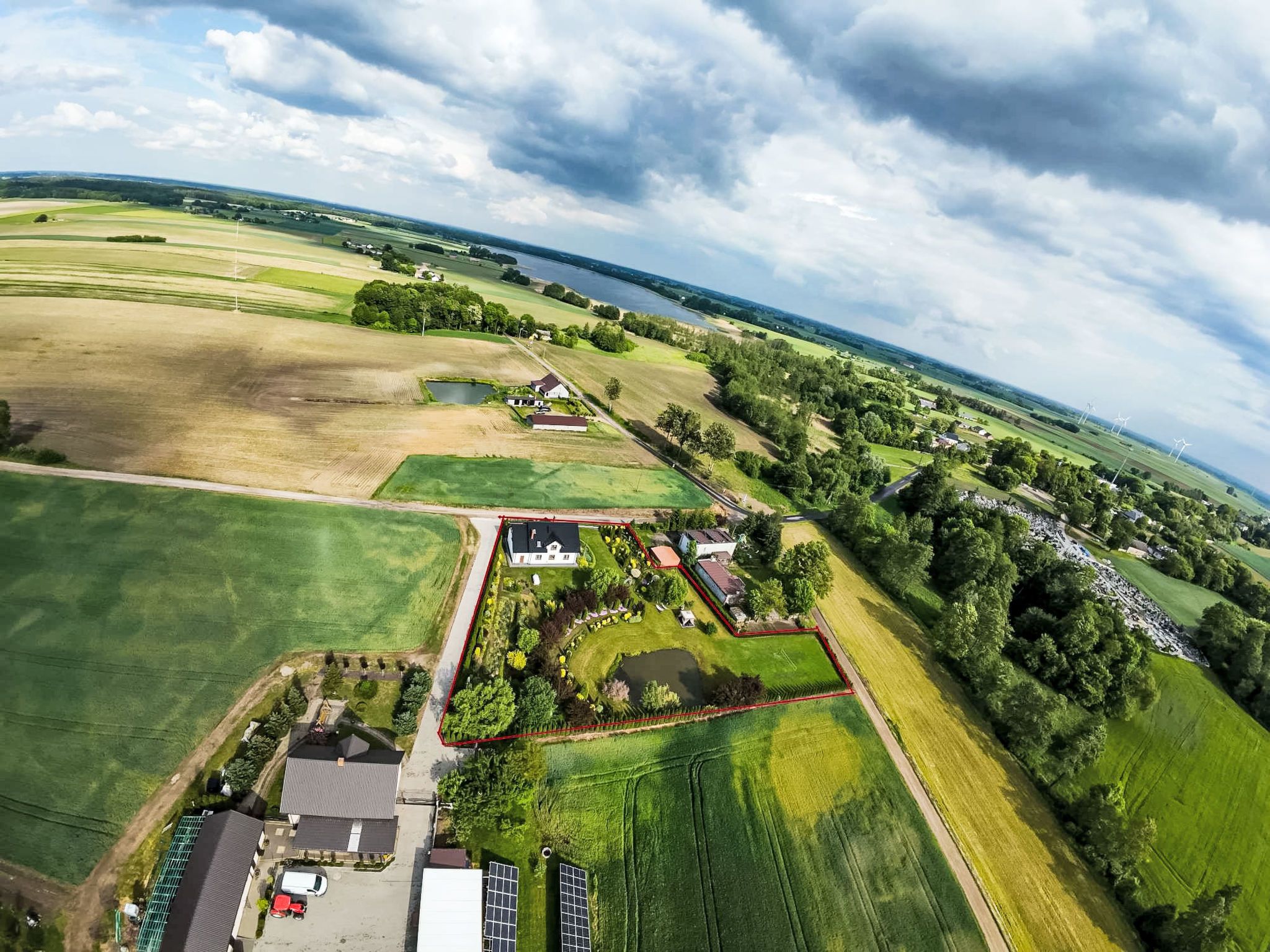 An aerial view of a rural property with fields, a pond, and wind turbines in the distance.