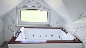 Une salle de bain moderne avec une baignoire sur pieds, une fenêtre donnant sur un paysage verdoyant et des murs à motifs de marbre.