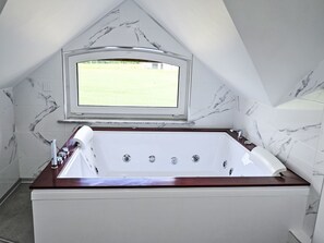 Un baño moderno con una bañera independiente, un ventanal con vistas a un paisaje verde y paredes con diseño de mármol.