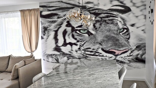 Un intérieur moderne avec un canapé, une table à manger et une grande fresque représentant un tigre sur le mur.