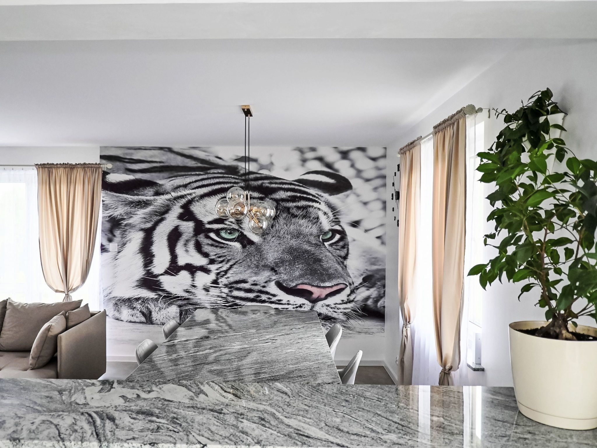 A modern living room with a large tiger mural, a marble coffee table, a sofa, and a potted plant.