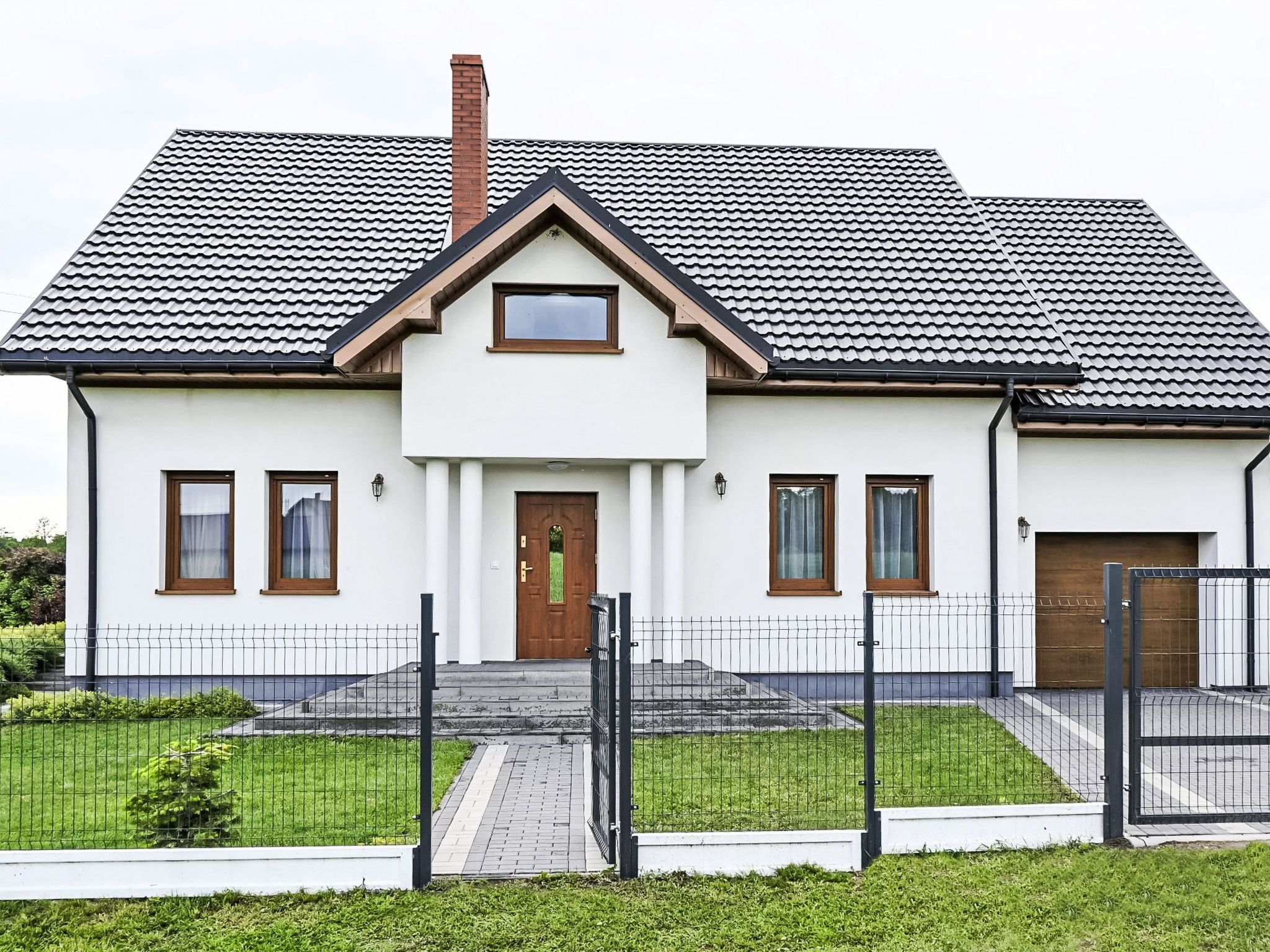 Une maison à deux étages, avec un toit recouvert de tuiles, une porte d’entrée et un petit porche.