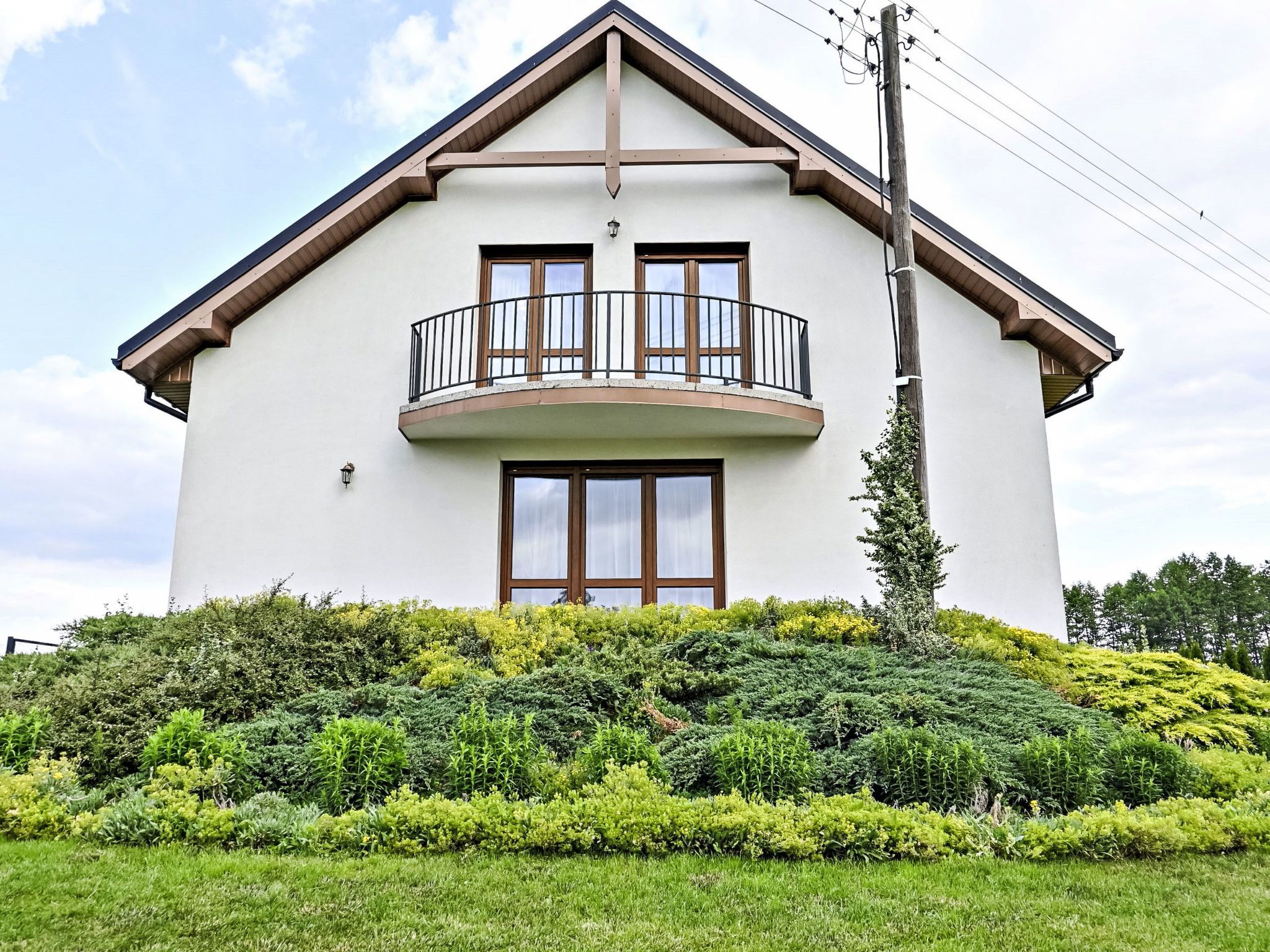 Une maison à deux étages dotée d’un balcon, entourée d’une végétation bien entretenue.