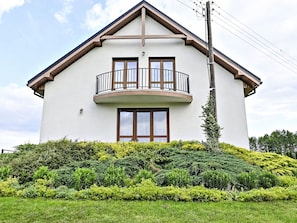 Una casa de dos pisos con balcón, rodeada de vegetación cuidada.