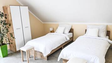 Un dormitorio con dos camas individuales, un armario de madera, una planta verde y un banco.