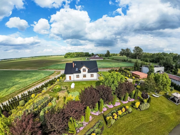 A large house with a well-maintained garden, surrounded by open fields and a clear sky.