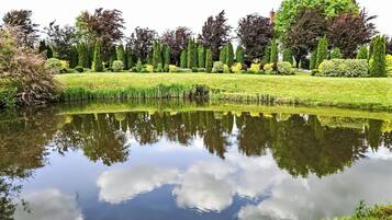 Un étang paisible dont les eaux reflètent clairement les arbres et le ciel, entouré de pelouses et de haies bien entretenues.
