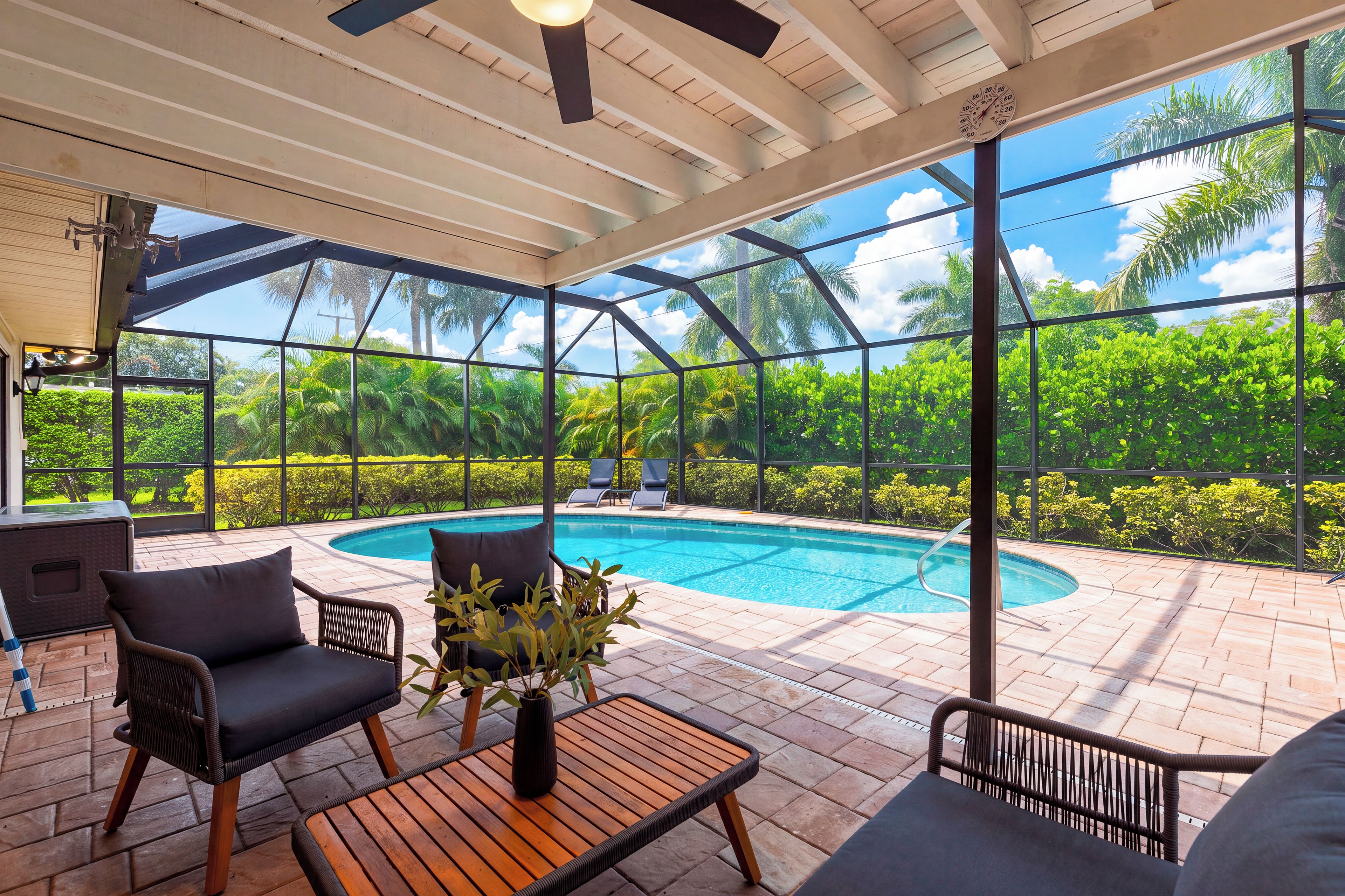 A covered outdoor area with a pool, lounge chairs, and a table with a vase of flowers.