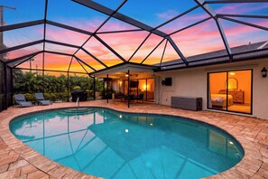 Ein Schwimmbecken mit Glasdach, umgeben von einer Terrasse mit Sitzgelegenheiten und Blick auf den Sonnenuntergang.