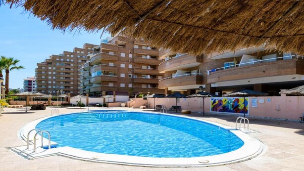Una piscina amb un teulat de palla, envoltada d'edificis de diversos pisos amb balcons.