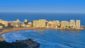 Paisatge urbà costaner amb edificis alts, una platja sorrenca i una roca al primer pla.
