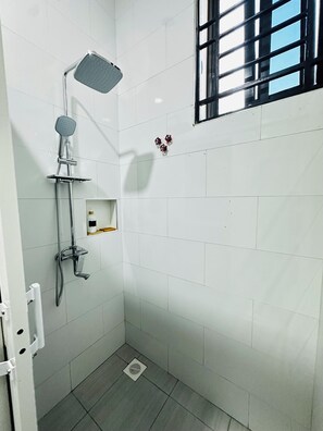 A small, tiled shower area with a handheld showerhead, a wall-mounted faucet, and a window with bars.