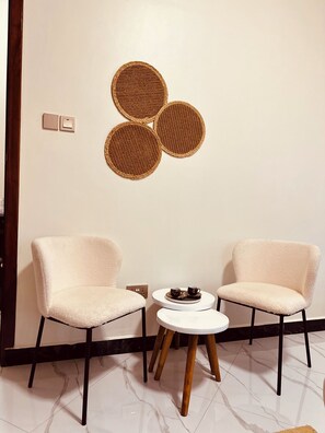 A room with two chairs, a small round table, and a wall-mounted woven art piece.