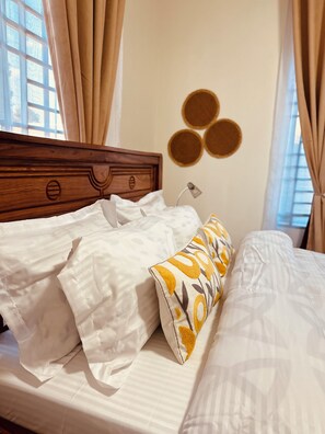 A neatly made bed with white linens and a decorative pillow, a wooden headboard, a bedside lamp, and a wall with circular decorations.