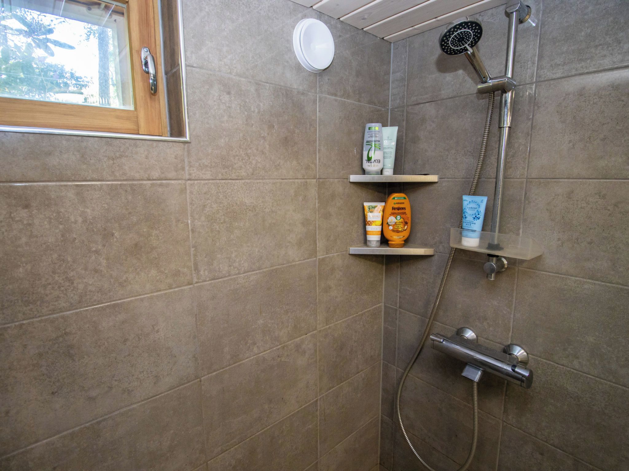 Eine Dusche mit Duschkopf und Duschschlauch. Es gibt Ablagen für Toilettenartikel.