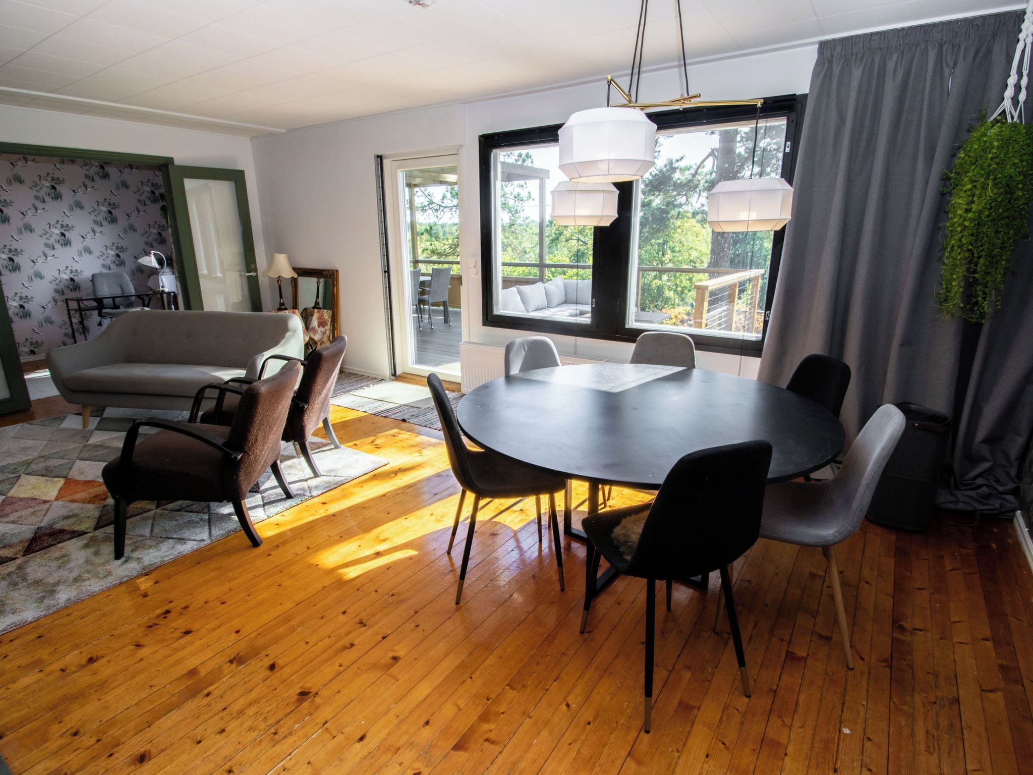Un espace de repas moderne avec une table ronde et des chaises, un canapé et une vue sur l’extérieur grâce à de grandes fenêtres.