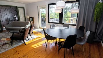 Un espace de repas moderne avec une table ronde et des chaises, un canapé et une vue sur l’extérieur grâce à de grandes fenêtres.