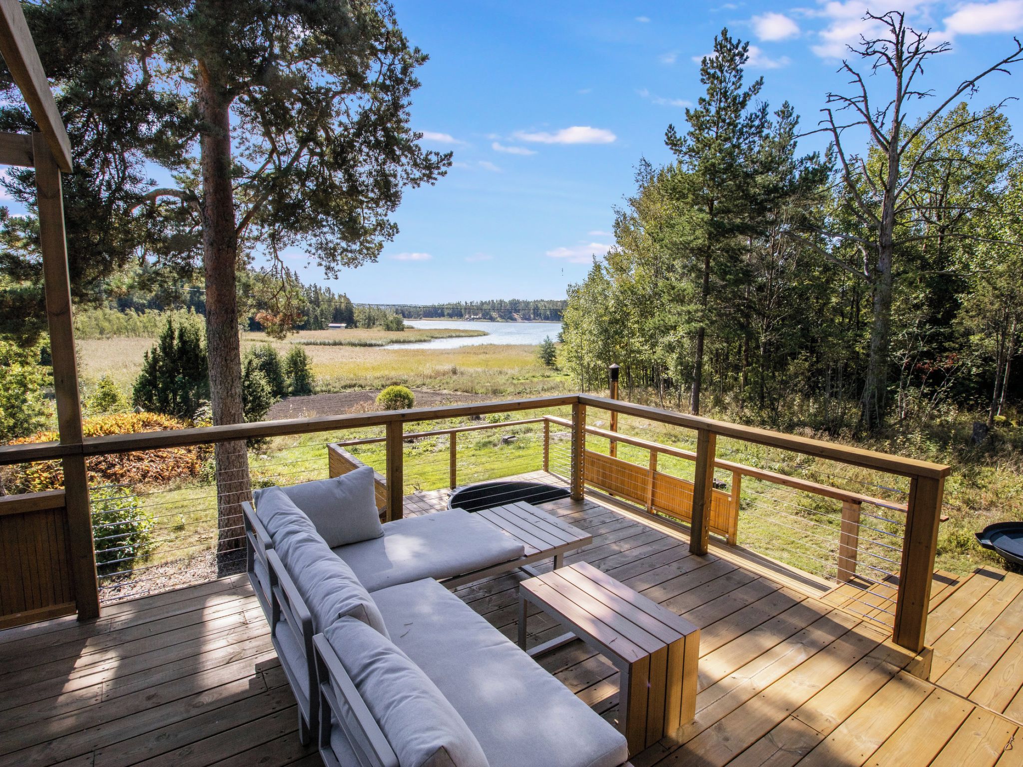 Eine Holzterrasse mit einer Couch und einem Tisch, mit Blick auf eine natürliche Landschaft mit Bäumen und einem Gewässer.