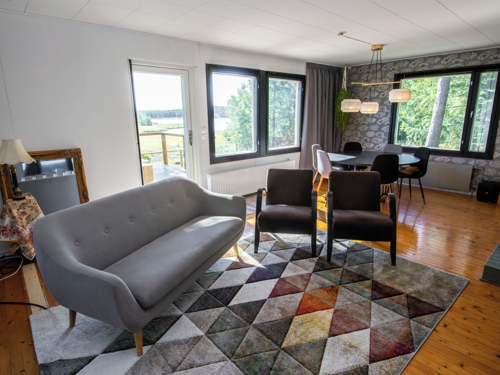 A modern living room with a grey sofa, two armchairs, a dining table with chairs, and large windows with curtains.