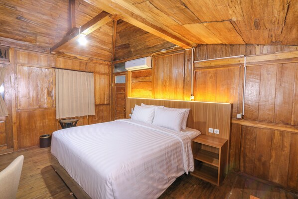 A wooden room with a bed, a nightstand, a small table, and a wall-mounted air conditioning unit.