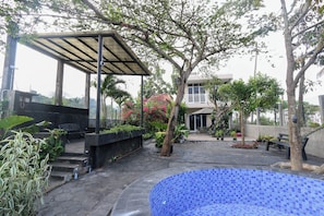 A covered outdoor area with a pool, surrounded by trees and potted plants.