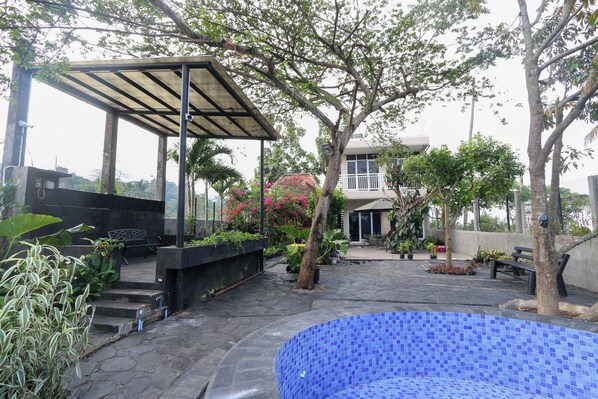 A covered outdoor area with a pool, surrounded by trees and potted plants.