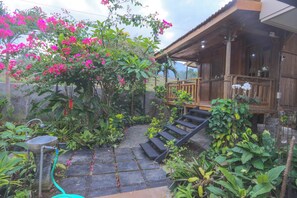 A wooden house with a porch, stone steps, and a garden with various plants and flowers.
