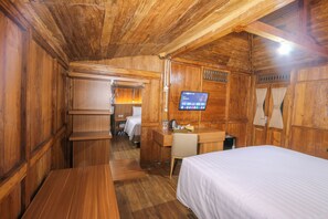 A wooden room with a bed, desk, and a television displaying a program.