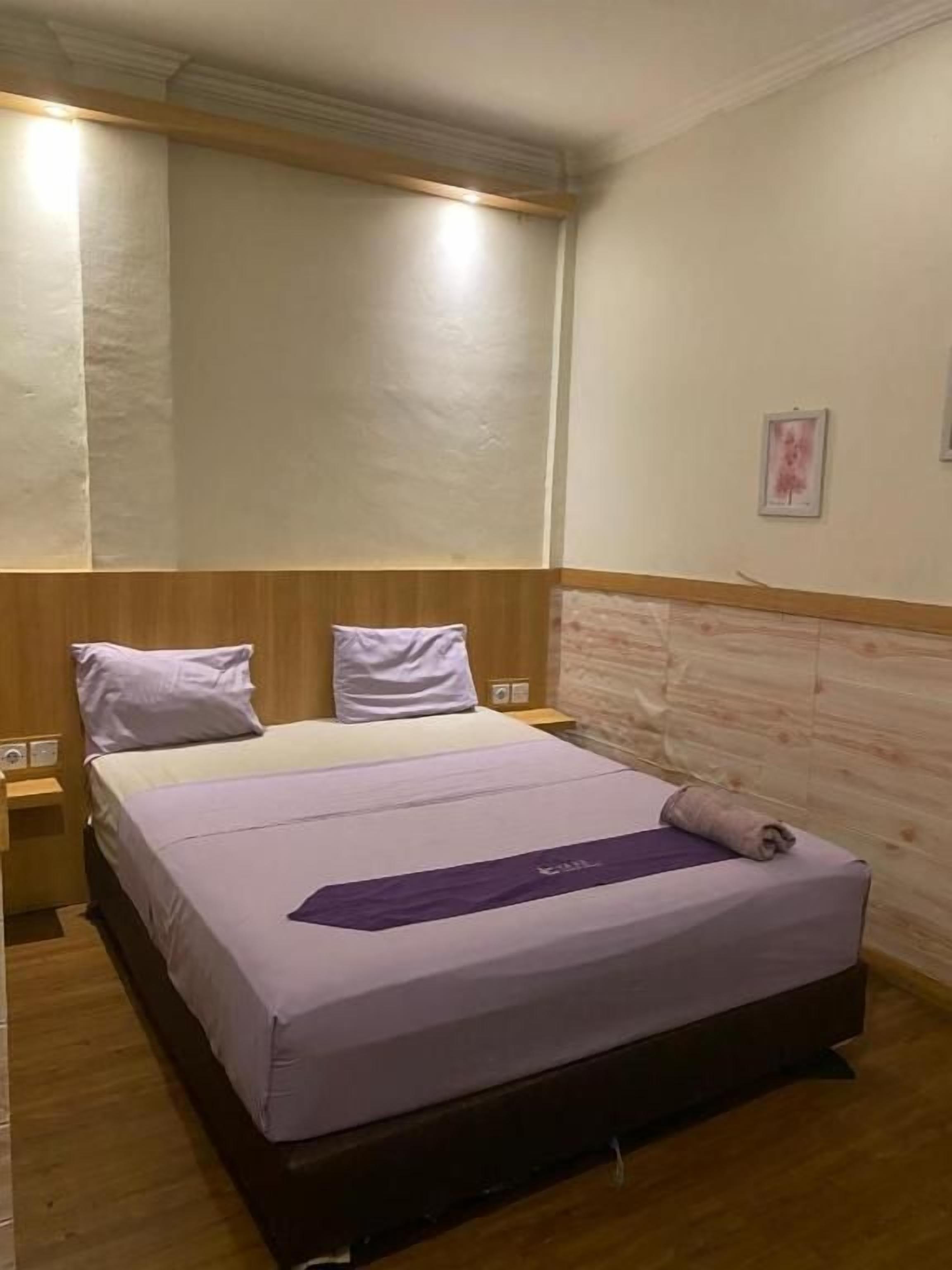 Une chambre avec un lit simple, une tête de lit en bois, une table de chevet et un luminaire fixé au mur.
