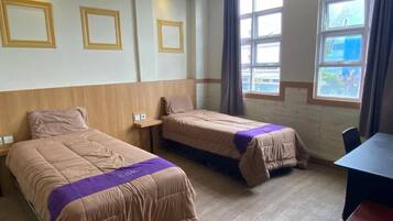 Habitación de hotel con dos camas, cabecera de madera, ventana con cortinas y una mesa.
