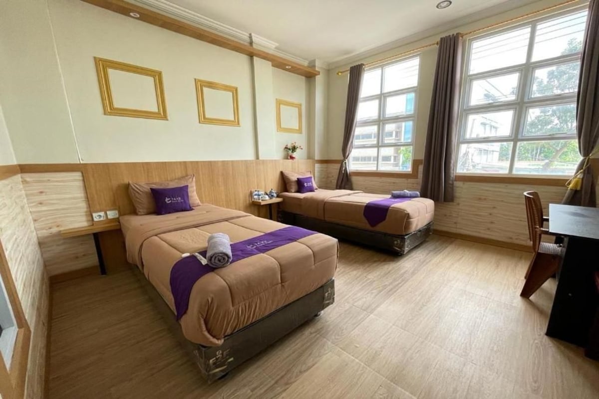 Een hotelkamer met twee bedden, een bureau en grote ramen.