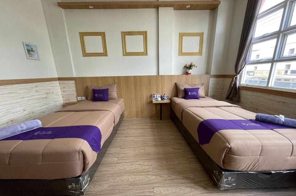 A hotel room with two beds, a small table, and a window with curtains.