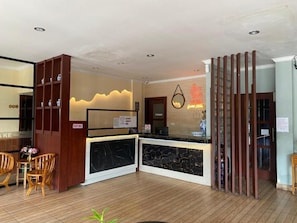 Een hotel receptie met een marmeren balie, houten stoelen en een decoratieve wand.