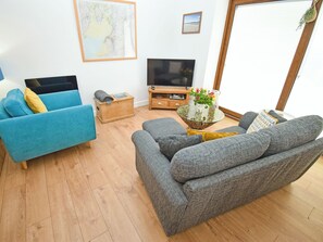 A living room with a sofa, a blue armchair, a wooden chest, a TV, and a small table with a vase of flowers. - 1 bedroom accommodation in Carr Bank, Arnside (Carr Bank, Arnside)