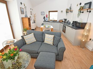 A modern living room with a grey sofa, a glass coffee table, and a vase with flowers. - 1 bedroom accommodation in Carr Bank, Arnside (Carr Bank, Arnside)