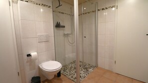 Ein Badezimmer mit Toilette, Duschkabine und Fliesenboden.