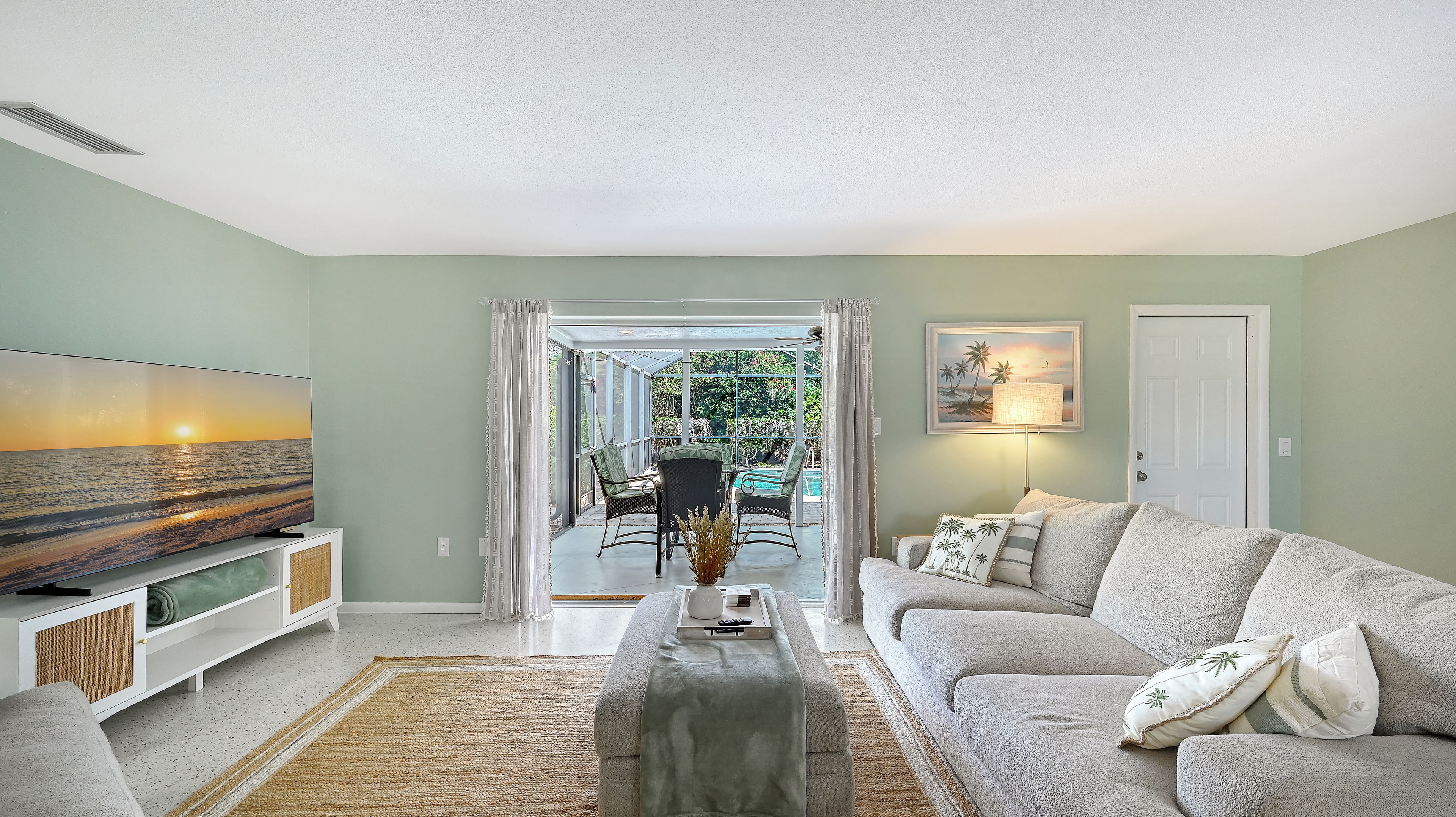 A living room with a sofa, TV, and a view of a pool and garden.