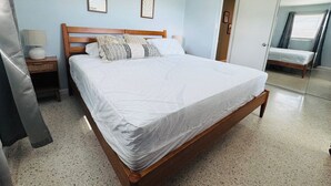 Een slaapkamer met een houten bed, een nachtkastje, een lamp en een deur naar een andere kamer.