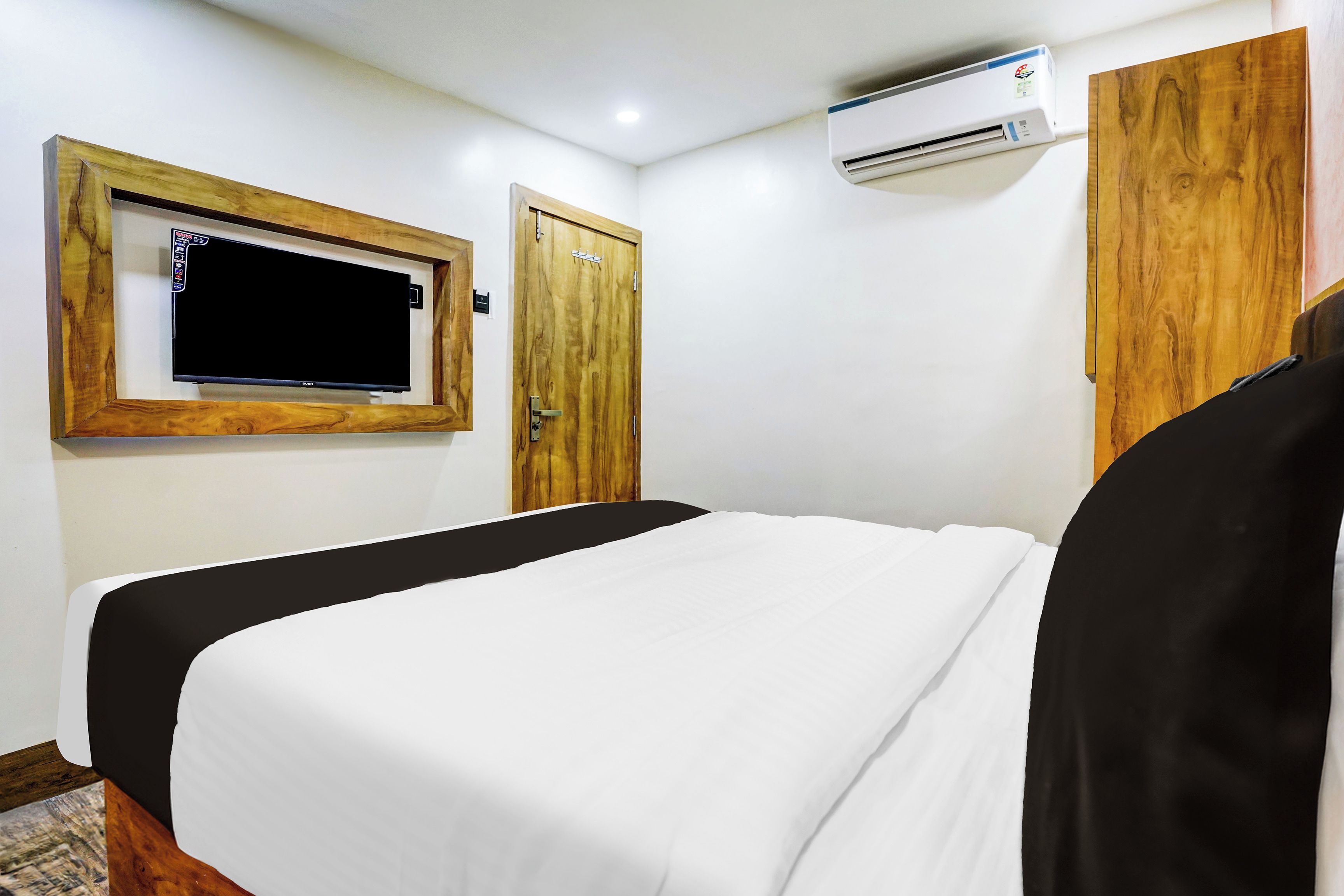 A hotel room with a bed, a television mounted on the wall, a door, and an air conditioning unit.