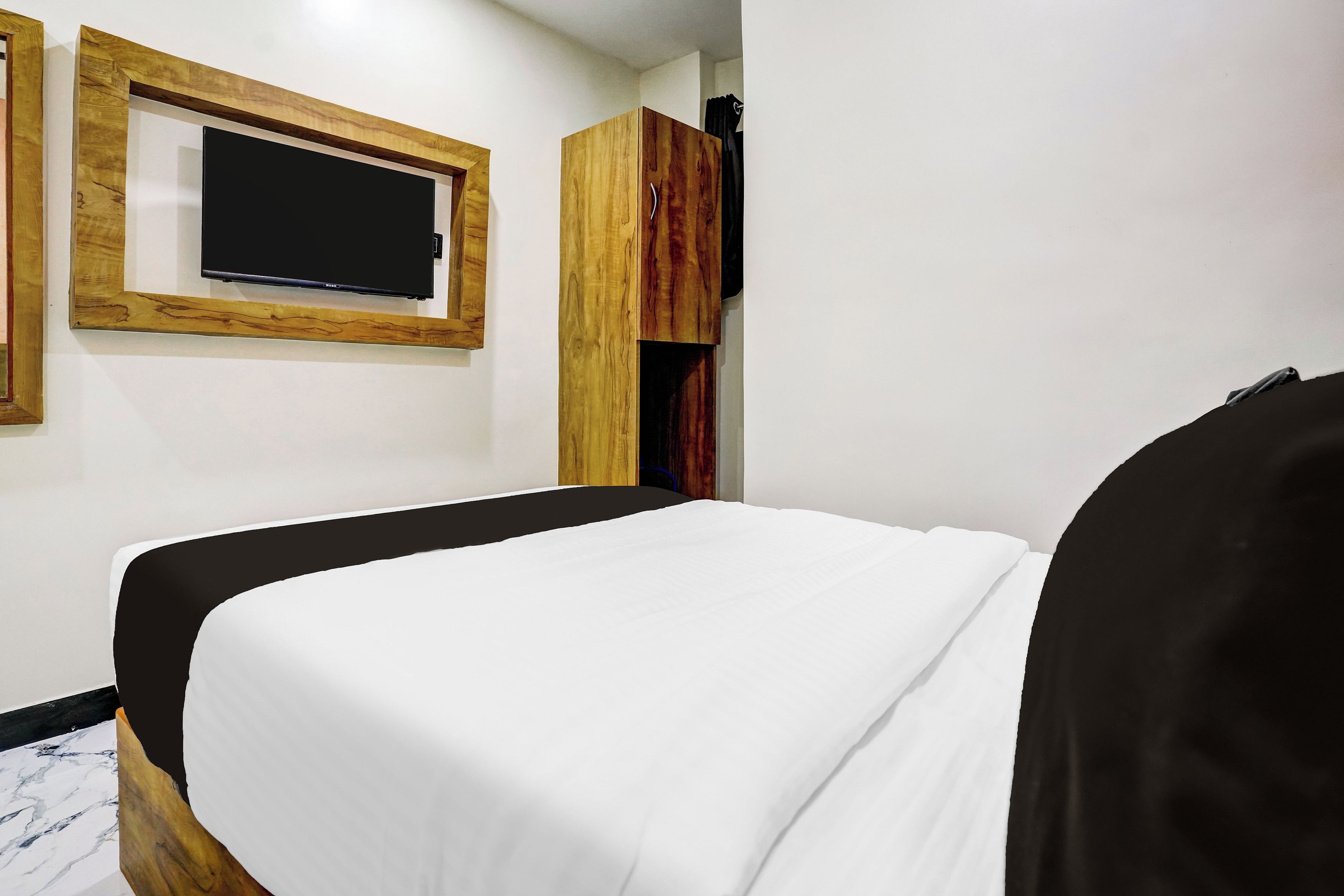 A hotel room with a bed, a television mounted on the wall, and a wooden wardrobe.