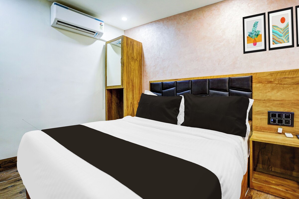 Habitación de hotel con cama, mesita de noche, espejo, equipo de aire acondicionado y obras de arte en la pared.